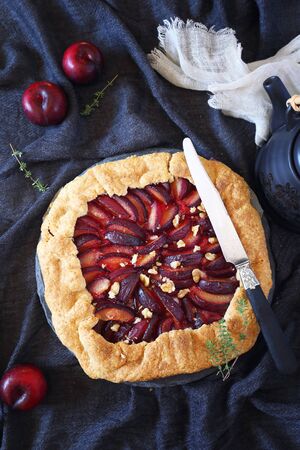 Homemade red plums tart galette with walnuts. Top view on dark backgroundの写真素材