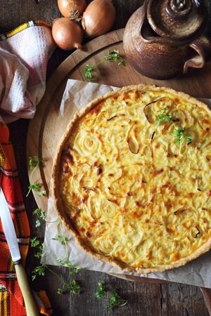French cuisine: onion creme tart on wooden chopping board, rustic style. Top view