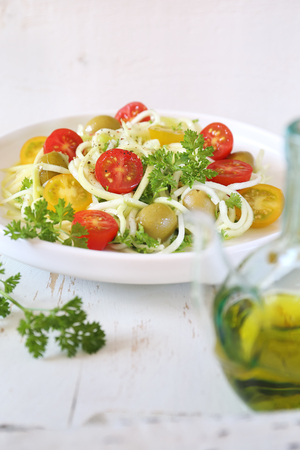 Vegetarian food: raw zucchini spaghetti salad with cherry tomatoes, olives, parsley and olive oil on light backgroundの写真素材