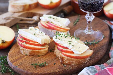 Apples and Camembert cheese bread toast and glass of red wine. Healthy savory sandwich on wooden cutting boardの写真素材