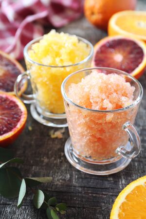 Orange granita, frozen summer dessert in two cups and  fresh orange fruits, selective focus on wooden backgroundの写真素材