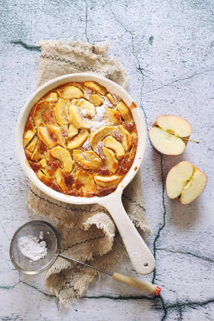 French cuisine. Apple clafoutis in ceramic dish for sweet dessert and fresh apples. Top view ongray light backgroundの写真素材