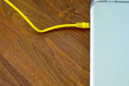 Closed laptop connected to  grey cable on brown wooden floorの写真素材