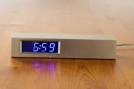 Digital alarm clock at 6:59 on wooden table