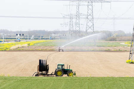 Elst, Netherlands - April 7, 2020: Tractor with irrigation equipment freshly seeded fieldのeditorial素材