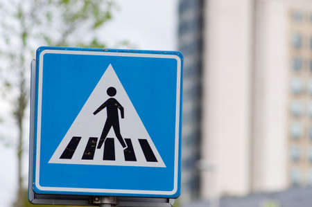 Blue pedestrian crossing sign with a building in the background in Arnhem, Netherlands