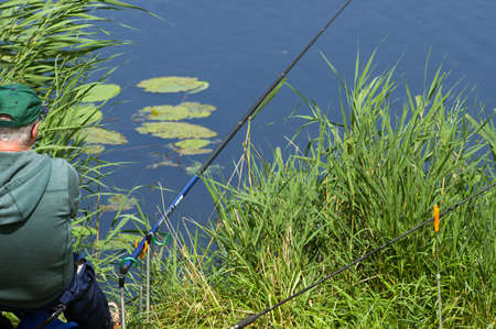 Doesbug, Netherlands - July 29, 2021: Man is fishing seen from behind on a quay of a lakeのeditorial素材