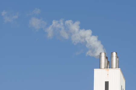 Closeup of a white industrial smokestack with white smoke a clear blue sky in the Netherlands