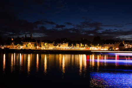 Cityscape of the center of Maastricht in twilight in the Netherlands with in the foreground the river Meuse and a streak of light from a passing boatのeditorial素材