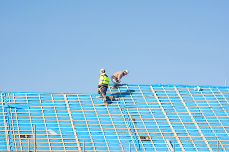 Nijmegen, Netherlands - February 8, 2023: Two workers at work on a roof under construction covered with blue plastic with a clear blue skyのeditorial素材