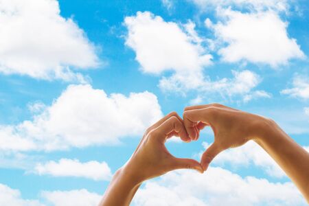Heart shaped hands on a background of clouds and sky, showing love.の写真素材