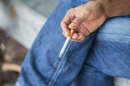 A young man sits on a smoking cigarette, destroying his own happiness.の写真素材