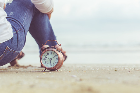 Alarm clock ringing on the beach during sunset. Part of the human body. Clock vintage style toneの写真素材