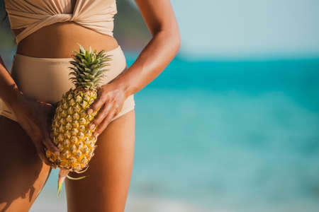 Fresh pineapple in hand beautiful woman on blurred outdoor sea background.の写真素材