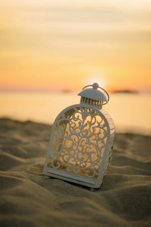 White decorative lantern on the beach at sunset. Vintage filter effect.