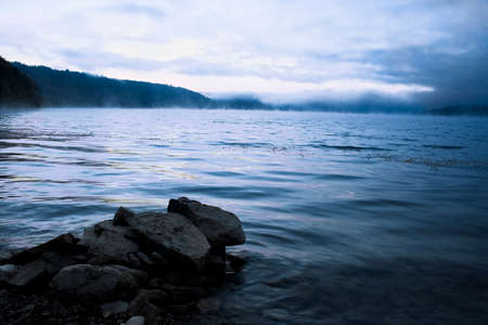 Beautiful water landscape with a fog above water & stones on a foreground. Image in blue, cold tone.の写真素材