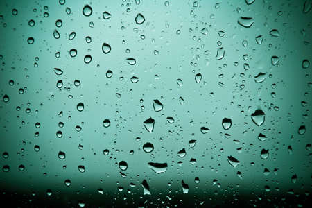 Cold cyan water drops over glass background with dark lower partの写真素材
