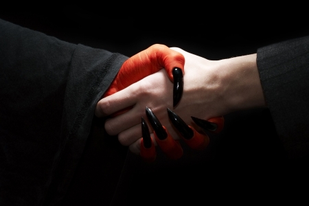 Economic conceptual image. Male businessman handshake with devil. Dark contrast lightingの写真素材