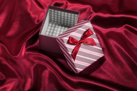 Empty gift box with red ribbon on red satin backgroundの写真素材