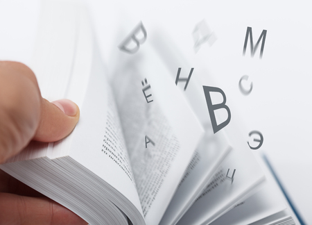 Letters flying with flipping book pages. Low aperture shot, selective focus. Education, reading, dictionary concept.の写真素材