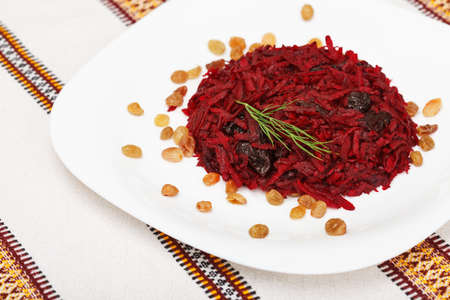 Grated beet salad with prunes and raisins, served on a white plate and home tableclothの写真素材