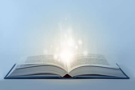 Abstract open magic book on table with light inside. Low aperture shot, focus on front part. Cold and warm toneの写真素材