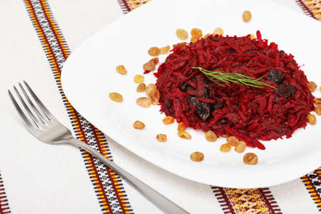 Grated beet salad with prunes and raisins, served on a white plate and home tablecloth with forkの写真素材