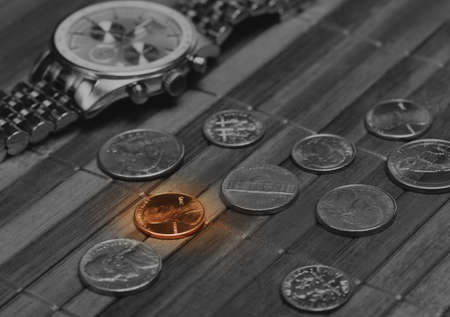 Watch with coins. Cost-is-no-object, time is money, poor income concept. Black and white image with colored part. Low aperture shot, focus on colored coinの写真素材