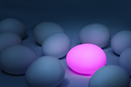 Pink glowing egg surrounded by usual ones. Standing out from the crowd concept, individuality...