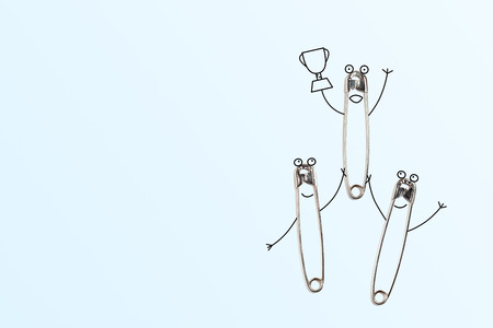 Three safety pins celebrating victory: two holding a winner with the cup in the hand. Funny cartoonish concept.の写真素材