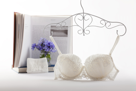 Elegant white bra and panties with flowers and book on background. Youth female underwear set, education themeの写真素材