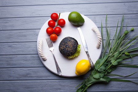 Black wooden serving tray with black burger, potato wedges and ketchup, vertical shot on a grey stone backgroundの写真素材