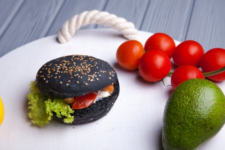 Black wooden serving tray with black burger, potato wedges and ketchup, vertical shot on a grey stone backgroundの写真素材