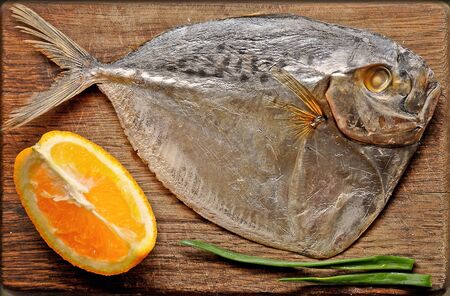 Dried fish, a slice of orange and green onions lying on a cutting board