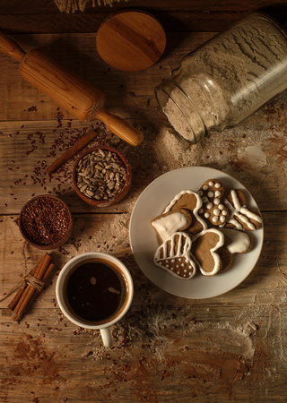 Decorated cookies on a saucer on a wooden table among the ingredientsの写真素材