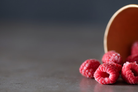 Frozen raspberries in the disposable cup on gray background. Place for text.