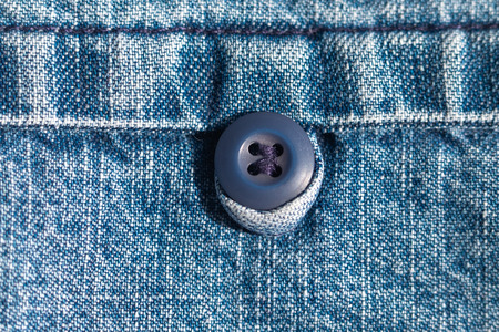 Denim closeup, the element of the pocket on which the round blue button. Textile concept.