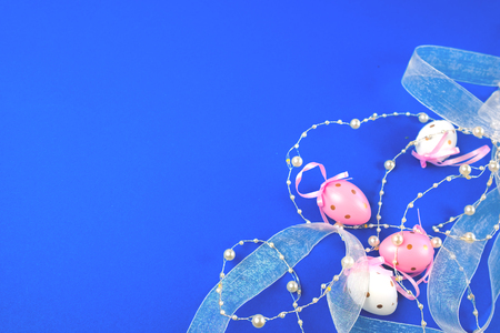 Easter egg decorated with ribbons and pearls on a blue background. Place for text.の写真素材