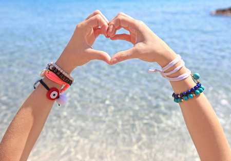 model advertising greek jewelry on the beach - creating heart symbol with her handsの写真素材
