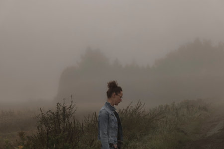 Young man standing in the middle of a foggy field in the countrysideの写真素材