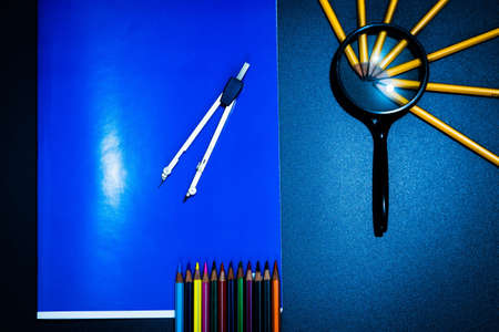 Concept of school or start of activities, office objects seen from above on a desk, pencil tips under a magnifying glass, a compass above a notebook and tips of visible colored crayons.の写真素材