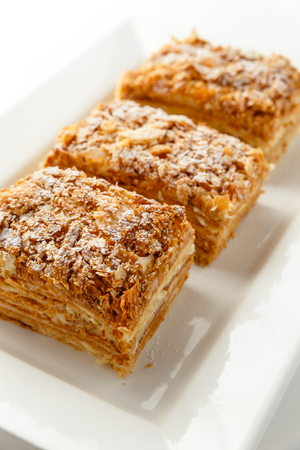 French Napoleon Cake of puff pastry with sour cream on a white plate close-up. Nutritious dessert. Selected Focus.の写真素材