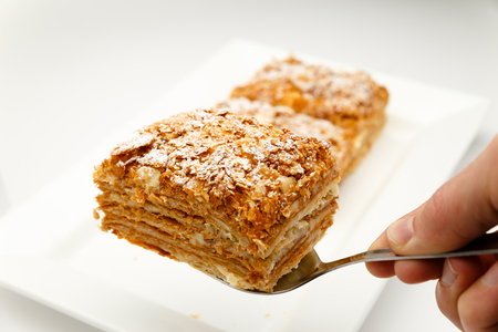 French Napoleon Cake of puff pastry with sour cream on a white plate close-up. Nutritious dessert....