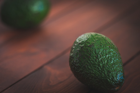 Two avocados on a brown wooden table.の写真素材