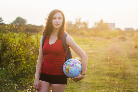 A girl with backback holding globe in sunset light backgroundの写真素材