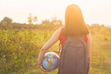 A girl with backback holding globe in sunset light backgroundの写真素材