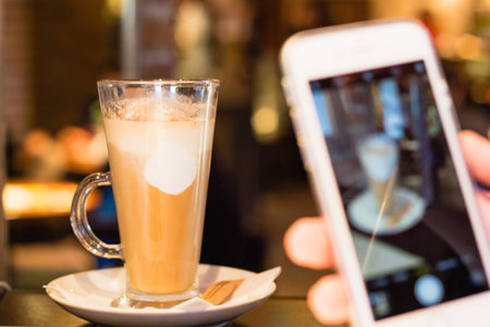 Taking picture of latte coffee with smartphone in cafeの写真素材