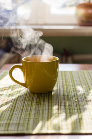 Steam of morning tea above yellow cup on tableの写真素材