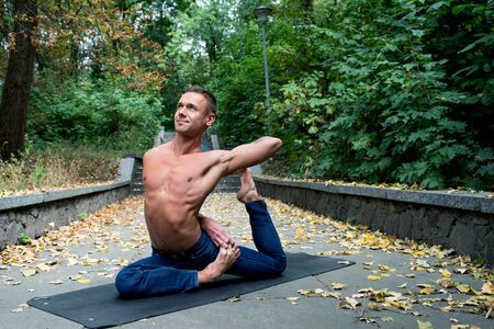 smiling Athletic man doing yoga asanas in the park on the hill at sunny day in the summerの写真素材