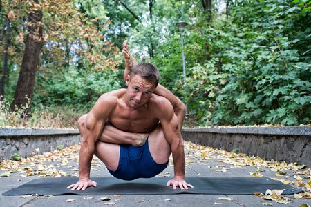 Handsome flexible Athletic man doing yoga asanas in the park in the fall